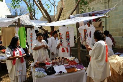 Puestos de artesanías con textiles y piezas en exhibición bajo una carpa