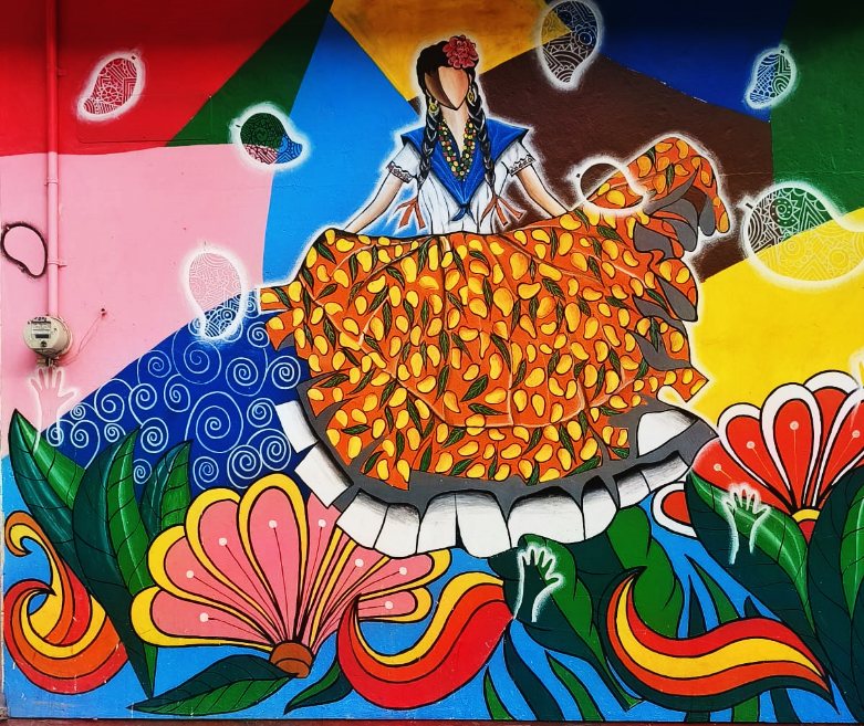 Mural de colores vivos con una mujer que porta falda floreada, pañoleta y trenzas, el traje tradicional de Cuicatlán