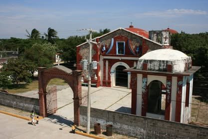 Templo de fachada roja y blanca detrás de una barda con arco de entrada