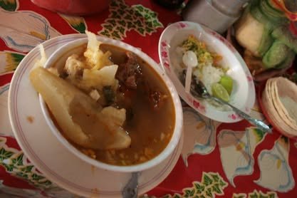 Plato de caldo con verduras y otros platillos sobre un mantel rojo