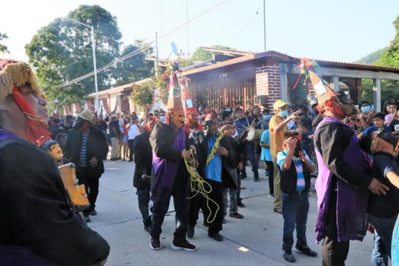 Fototeca Procesión por la calle del pueblo: participantes con capas moradas y tocados ceremoniales.
