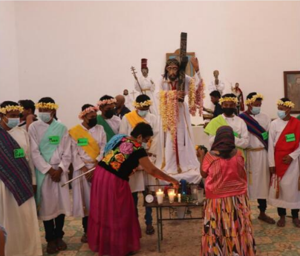 Fototeca Interior del templo durante una ceremonia, con imágenes religiosas y participantes con vestimenta ritual.
