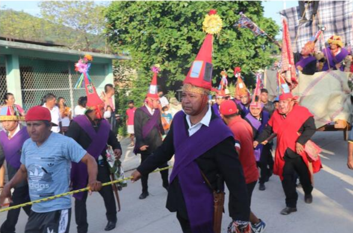 Fototeca Comparsa avanzando por la calle con gorros cónicos rojos y capas moradas.