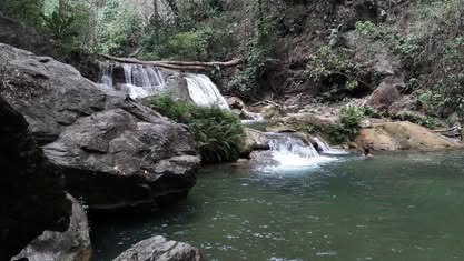 Cascada que cae entre rocas grandes hacia una poza verde
