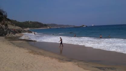 Mazunte y Punta Cometa: infraestructura turística de un Pueblo Mágico Playa de arena con olas y acantilados al fondo