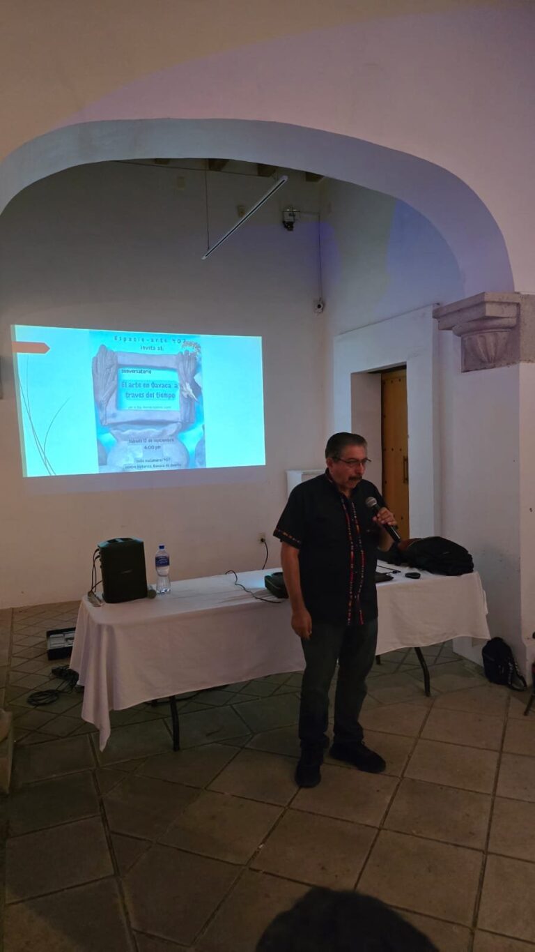 El Dr. Marcos Pedro Ramírez López, de pie junto a la mesa del proyector, presenta frente a la pantalla