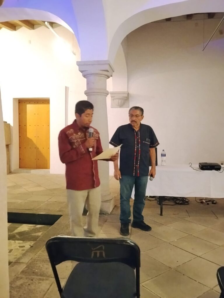 El Dr. Marcos Pedro Ramírez López, ponente en el conversatorio «El arte en Oaxaca a través del tiempo», en Mitla Un representante de los organizadores lee la constancia de participación junto al Dr. Marcos Pedro Ramírez López