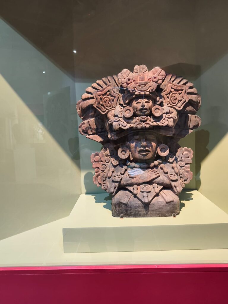 El Dr. Marcos Pedro Ramírez López, ponente en el conversatorio «El arte en Oaxaca a través del tiempo», en Mitla Urna efigie zapoteca de cerámica con tocado elaborado, exhibida en vitrina