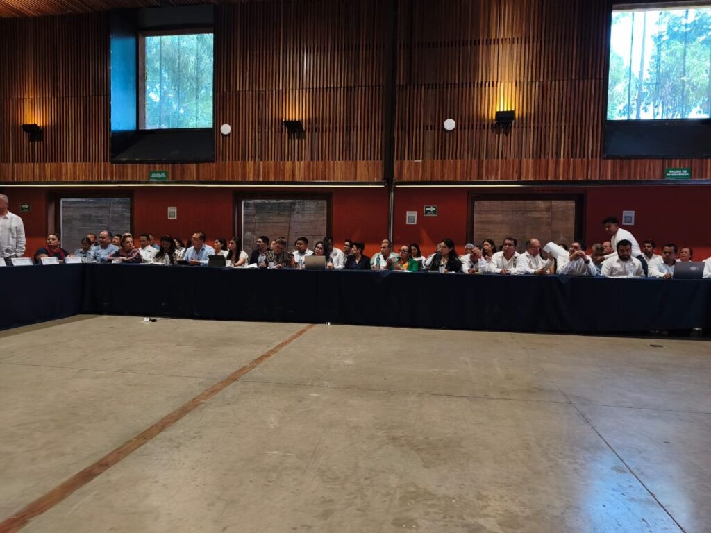 El grupo de turismo comunitario en NECTLI, la reunión regional Sur-Sureste del TecNM Vista amplia de la sala con decenas de participantes sentados alrededor de mesas con mantel azul