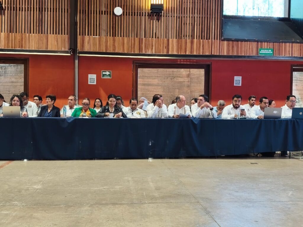 El grupo de turismo comunitario en NECTLI, la reunión regional Sur-Sureste del TecNM Fila de participantes en una mesa larga, algunos con computadoras y documentos