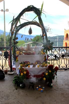 Arco adornado con flores y hojas sobre una mesa con ofrendas