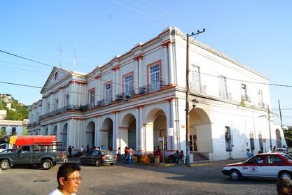 Memoria de campo 2011–2026 Palacio municipal blanco de dos plantas con arcos, frente a una calle con autos