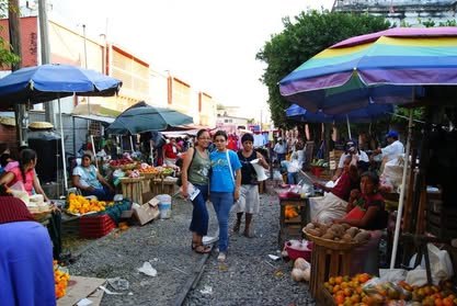 Mercado al aire libre con sombrillas de colores, puestos y gente comprando