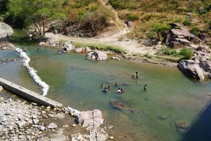Poza de un río entre rocas claras, con bañistas a lo lejos