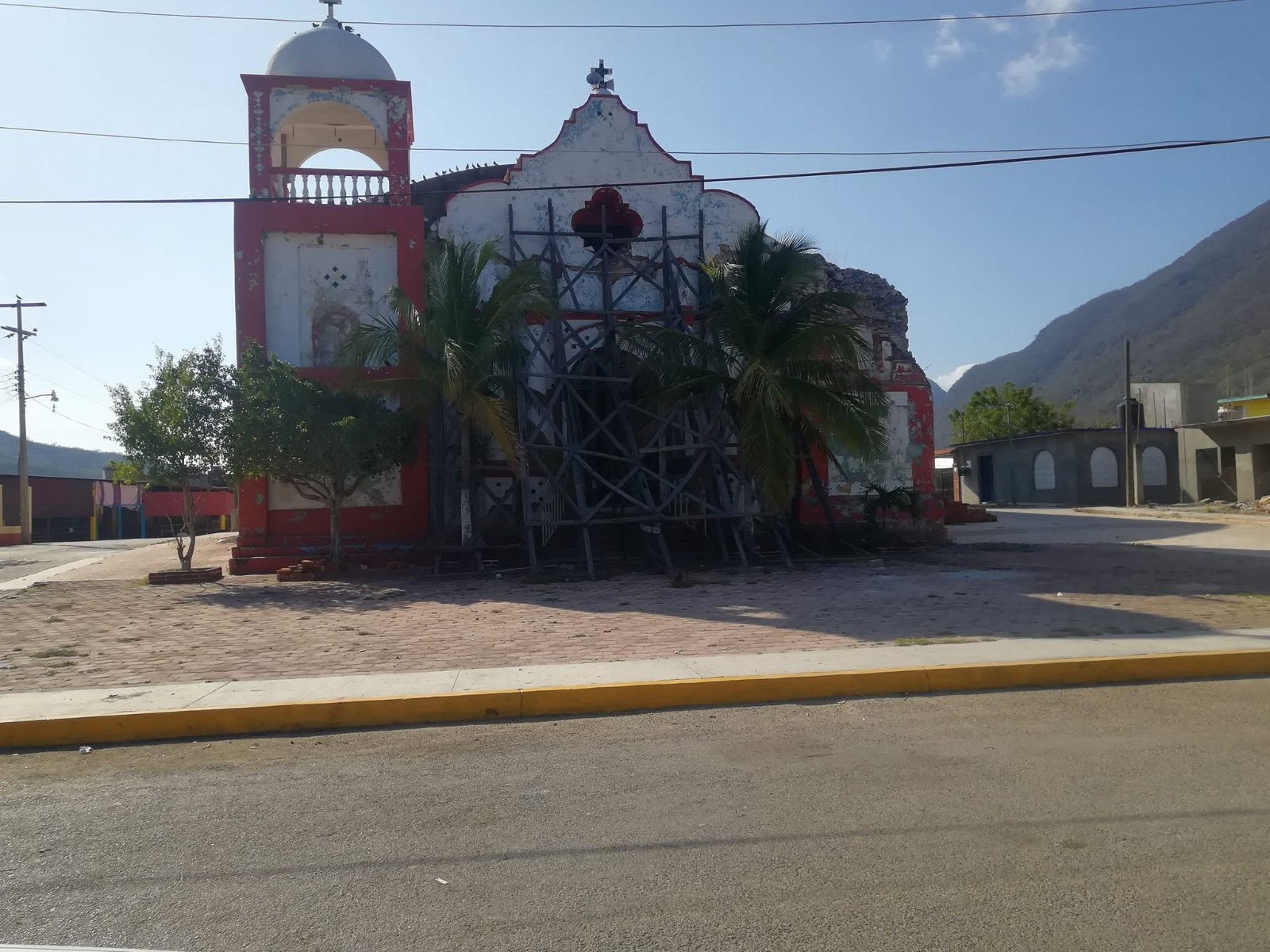 Templo de fachada clara con torre, frente a una calle amplia y cerros al fondo