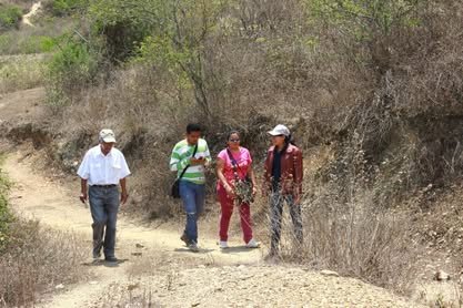 Tres personas caminan por una vereda de tierra entre arbustos secos