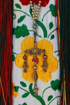 Detalle de un huipil blanco bordado con flores de colores y una cruz de plata colgada