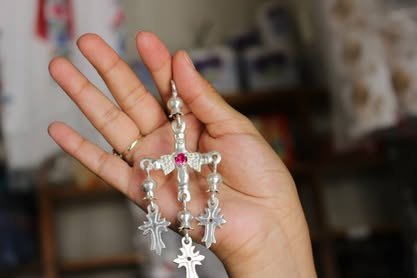 Mano abierta que sostiene una cruz de plata con colgantes, propia de Yalálag